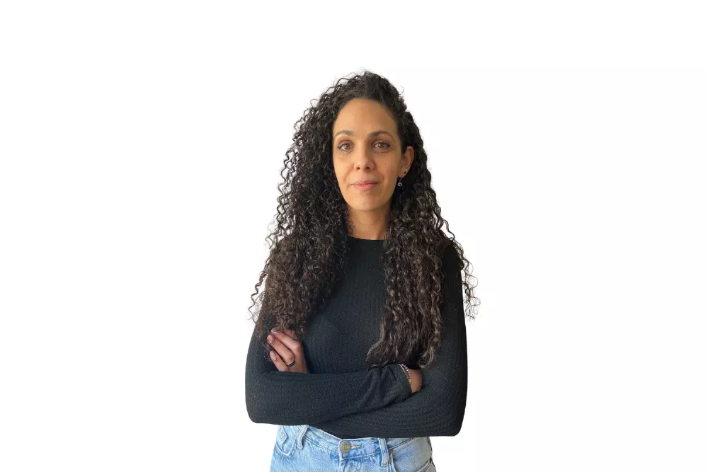 Mujer sonriendo con brazos cruzados, fondo blanco.