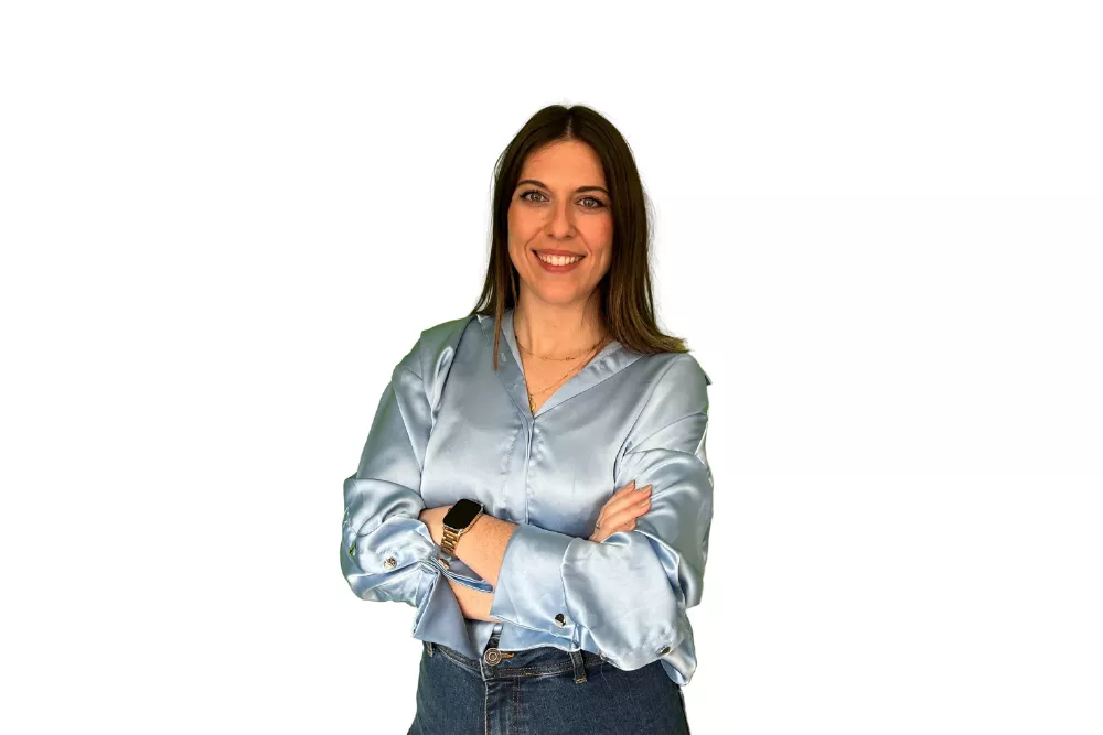 Mujer sonriendo con brazos cruzados, fondo blanco.