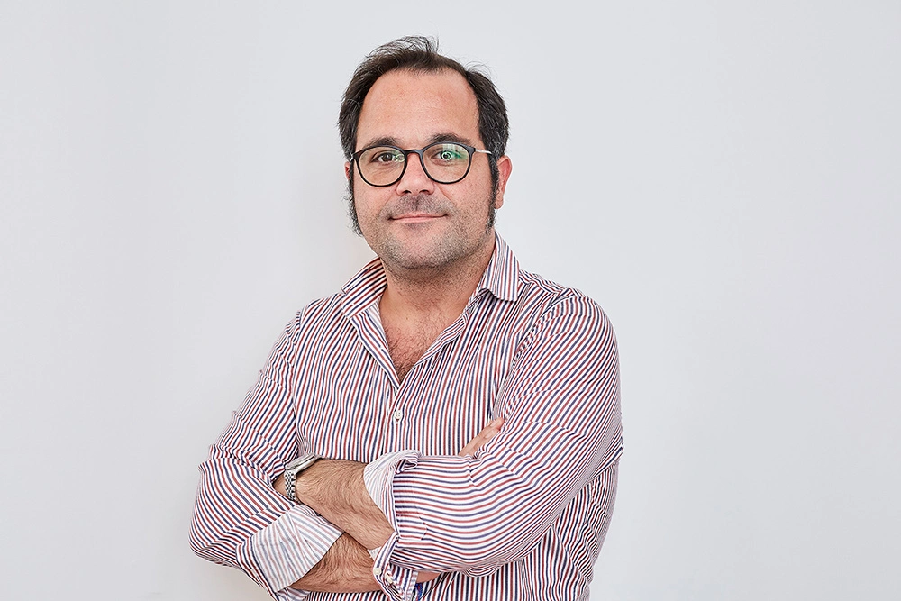 Hombre sonriendo con brazos cruzados, fondo blanco.